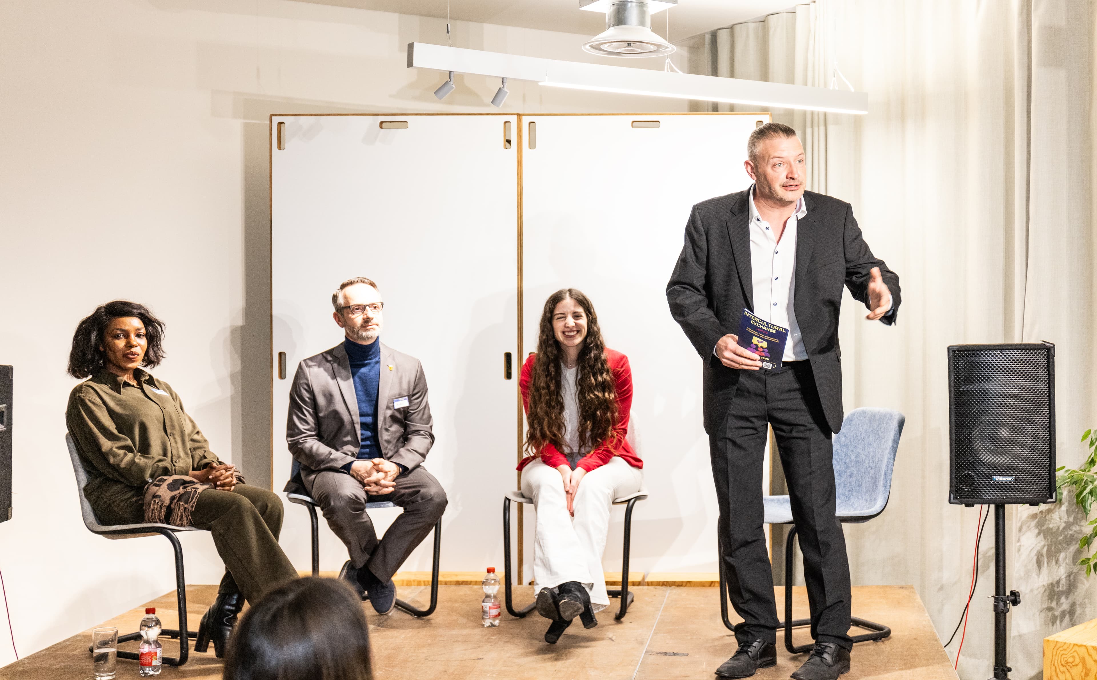 Dirk Brueckner seated, gesturing thoughtfully during a panel