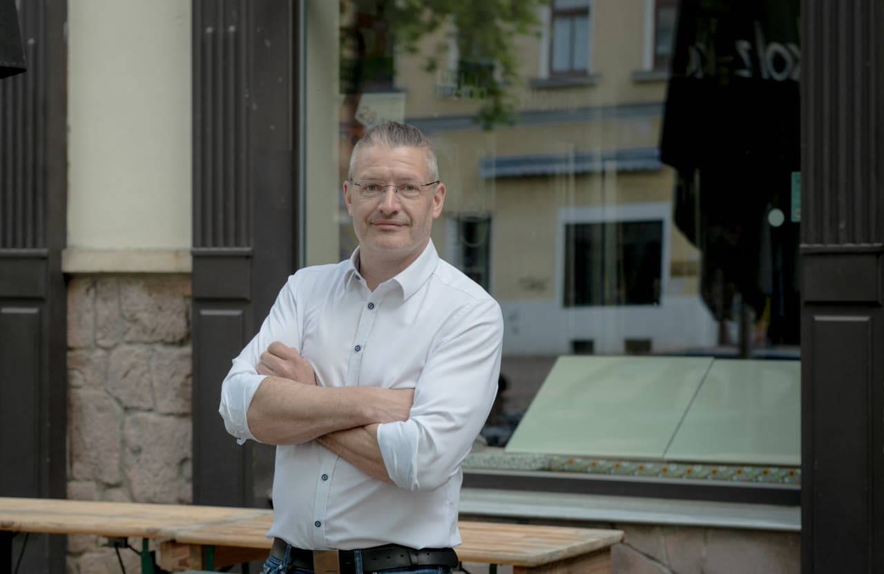 Portrait of Dirk Brueckner standing outside a café, arms crossed